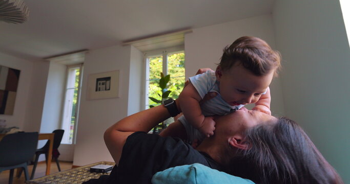 Mother lifting baby into the air while playing, smiling and laughing in a bright living room filled with natural light, joyful moments of bonding and love between mother and child