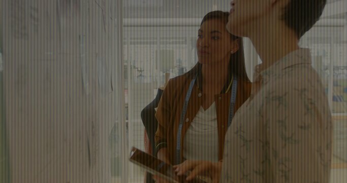 Designers examining sketches on whiteboard in studio, holding tablet and swatch with measuring tape