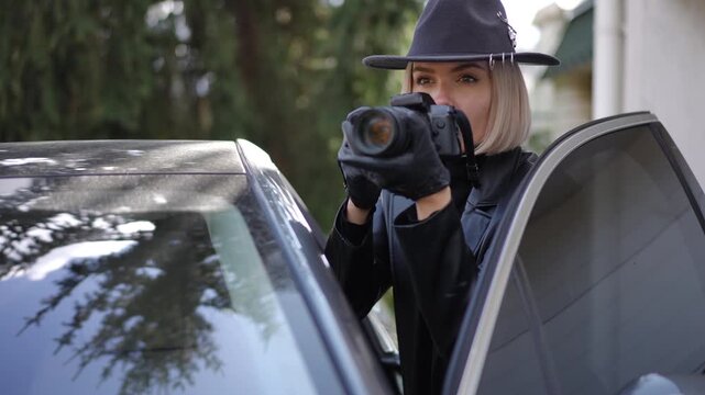 A female detective in black leather coat and hat secretly observes surroundings with camera from car, documenting evidence for investigation.