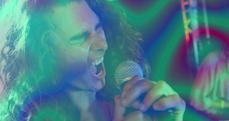 Singing curly-haired singer belting into microphone on club, with stage lights, truss and drum kit