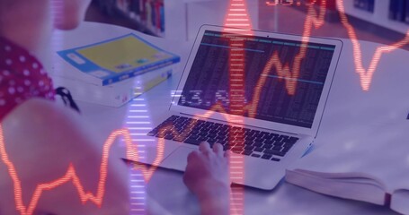 Typing teenager in red viewing charts on laptop with open book at white desk, copy space