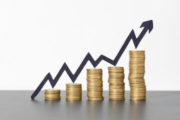 Stacks of coins and rising arrow on gray background indicating positive financial growth, business success concept. Copy space