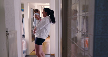 Mother holding baby in hallway with reflection on tiles, candid authentic lifestyle scene, intimate family moment, nurturing and bonding, warm and natural light