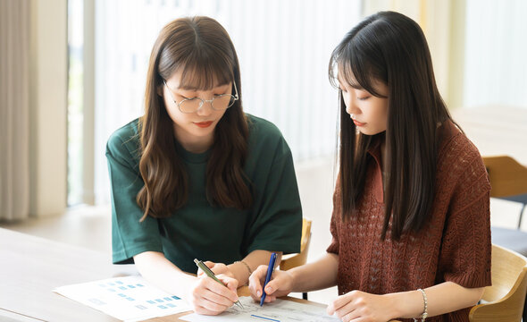 資料を見ながら打ち合わせをする2人の女性 - Powered by Adobe
