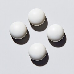 Four perfectly round, off-white spheres arranged symmetrically on a light gray surface.  Shadows cast beneath each sphere