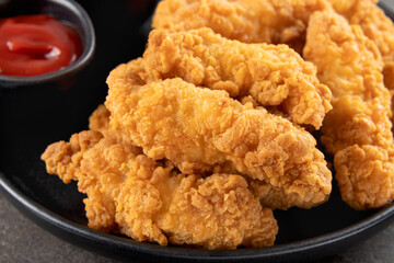 Crispy chicken breast strips with ketchup on a dark background. Close-up. Fast food.