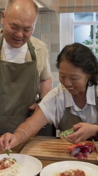 Vertical video: Once plated Senior couple seasoning, drizzling olive oil before dancing in kitchen
