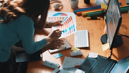 Top down view of smart designer helping manager choosing color from colored palettes. Aerial view of businessman working together and planning together while looking at logo from laptop. Symposium.