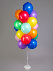 Multicolored balloons on white plastic stand isolated on gray background