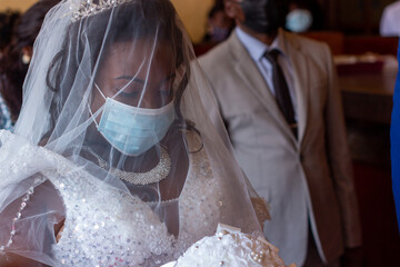 African Bride in Focus with Groom Beside, Both Wearing Disposable Face Masks