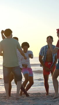 Vertical video: Diverse friends dancing on sandy beach at sunset after music beat cueing clapping