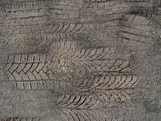 Close-up of multiple tire tracks imprinted on hot asphalt during summer heat, showing detailed tread patterns, vehicle traces, and textured road surface
