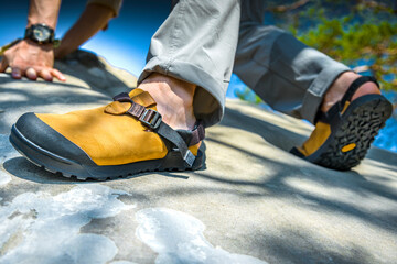 Man climbing rock in yellow hiking sandals, durable outdoor footwear for trekking and adventure travel