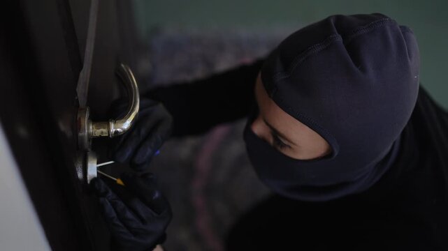 A person wearing a mask is attempting to pick a lock, indicating a possible breakin scenario that could occur