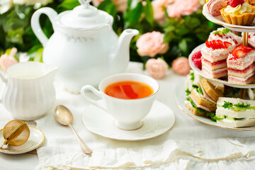 Afternoon tea table. Assortment of cakes, sweets and sandwiches. Rose garden background. Close up.