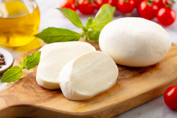 Fresh mozzarella cheese with cherry tomatoes and basil leaf on a cutting board. Marble background. Close up.