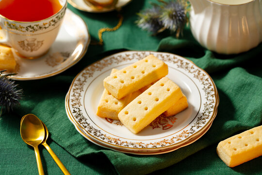 Shortbread cookies on a plate with cup of tea. Traditional Scottish dessert. Green textile background.