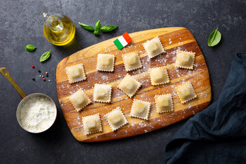 Ravioli on wooden cutting board with Italian flag. Dark background. Top view.