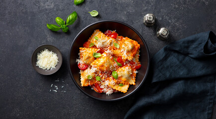 Ravioli with cheese, tomato sauce and fresh basil in black bowl. Dark background. Top view.