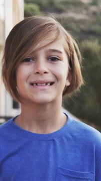 Smiling boy aged eight standing outdoors on porch, wearing bright blue t-shirt with chest pocket