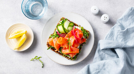 Salmon sandwich, toast with fresh cucumber, pickled onion, cream cheese and arugula salad. Light grey background. Top view.
