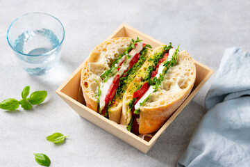 Ciabatta sandwich with mozzarella cheese, fresh tomatoes and basil pesto sauce in wooden box. Grey background. Close up. Top view.