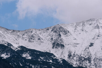 snow covered mountains tatry poland with clouds around and big pine trees