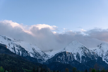  spring time sharp peaks rocky high snow covered mountains with cloudy sky landscape with green forest around