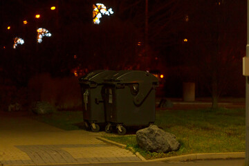 A captivating and vivid image of trash bins situated in a dimly lit urban area, subtly illuminated by distant street lights, showcasing a typical yet intriguing nighttime city environment