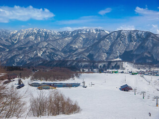 A wide ski slope with chairlifts, a restaurant and a pond at middle of Tsugaike Mountain Resort (Hakuba, Nagano, Japan)
