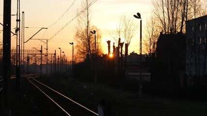 Sunset over train tracks and an urban landscape with industrial buildings and power lines.