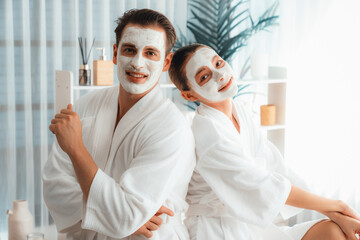 Blissful couple in bathrobe with facial cream mask enjoying serene ambiance of spa salon resort or...