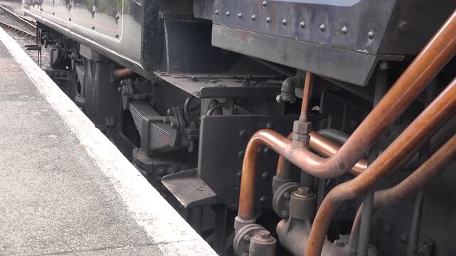 Close up of steam train wheels turning as locomotive moves away from a station as tourists take heritage transport in England UK 4K