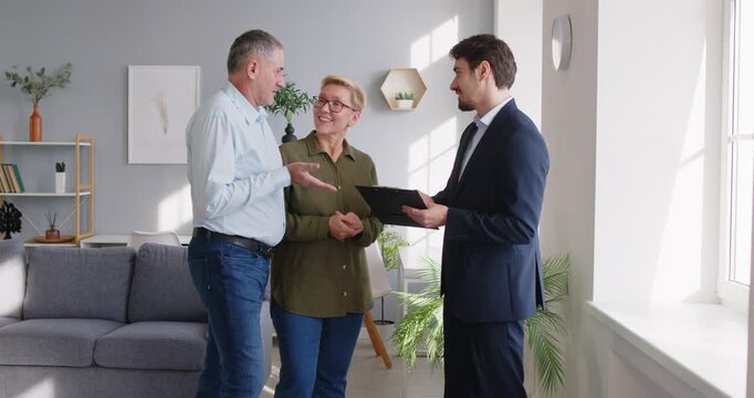 Professional realtor talking to senior couple standing at home and explaining contract details. Elderly clients attentively listening, discussing real estate deal or investment plan and shaking hands. - Powered by Adobe