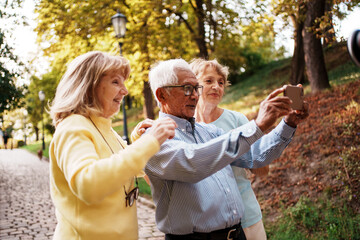 Joyful older adults happily taking a fun selfie together in a beautiful autumn park setting