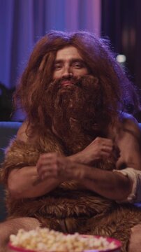 Prehistoric time traveler wild caveman in animal fur pising at camera smiling looking confident staying in modern apartment house. Homo sapiens. Human evolution.