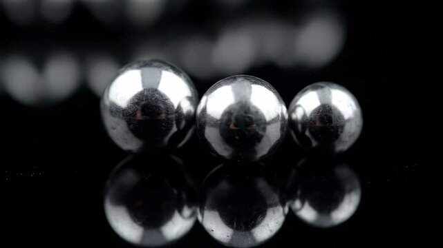Close Up Metal Ball Bearings on Black Reflective Surface - Extreme close-up shot of several metallic ball bearings resting on a reflective black surface.