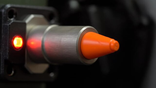 Industrial Proximity Sensor Close-up - A detailed close-up shot of an industrial proximity sensor. The sensor features a metallic body, an orange tip, and a red indicator light which is illuminated,