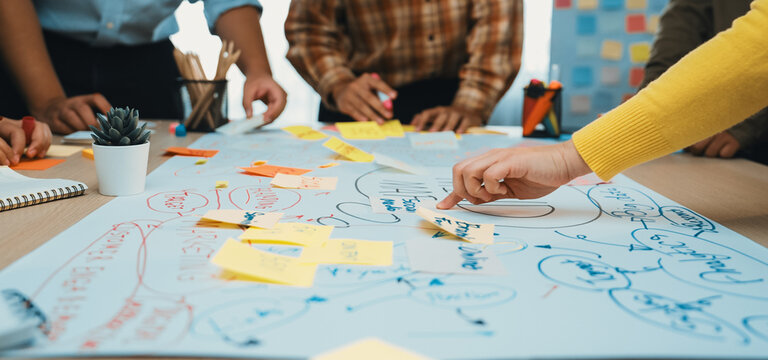 A diverse team engages in a lively brainstorming session, using sticky notes and large paper to generate and organize creative ideas in an inspiring office setting. SACTR