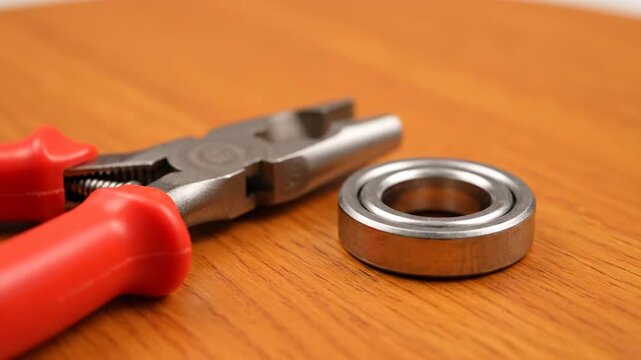 Red-Handled Pliers and Retaining Ring on Wood - Close-up shot of red-handled snap ring pliers positioned next to a circular retaining ring on a light brown wooden surface.