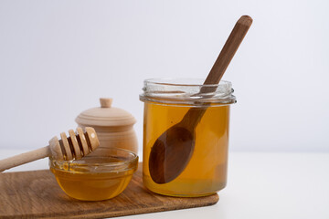 Jar of honey with wooden honey dipper on white kitchen background. Tasty honey bunker.
