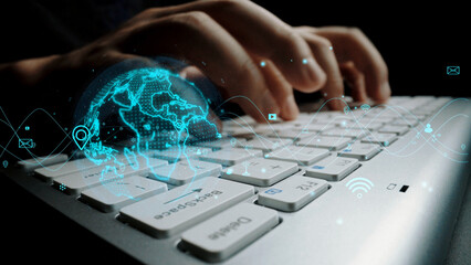 Close-up view of hands typing on a sleek keyboard, enhanced with a digital overlay of a global map and connectivity icons symbolizing technology and communication. Xenic
