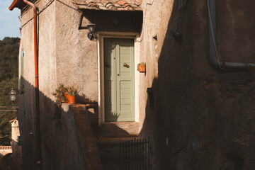 Rustic Mediterranean alley with old pastel green door and terracotta pot in warm afternoon light.