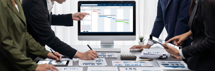 Panorama shot analyst team utilizing BI Fintech to analyze financial report with laptop. Businesspeople analyzing BI data dashboard displayed on laptop screen for business insight. Prodigy