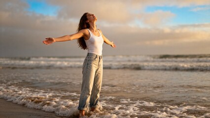 Smiling woman enjoying the beach with arms outstretched, standing in shallow water, feeling the ocean breeze at sunset.