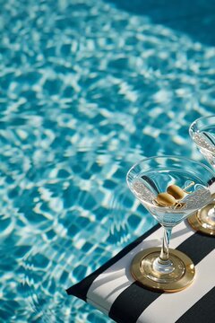 Two classic martini cocktails with olives by a sparkling swimming pool