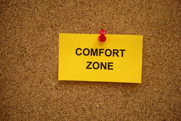 A yellow paper note with the words Comfort Zone on it pinned to a cork board. Close up.