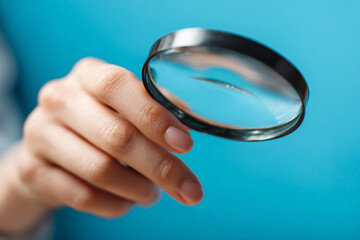 A hand holds a magnifying glass against a blue background a close up shot