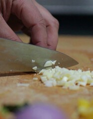 A chef's hand using a knife to finely chop garlic on a wooden cutting board