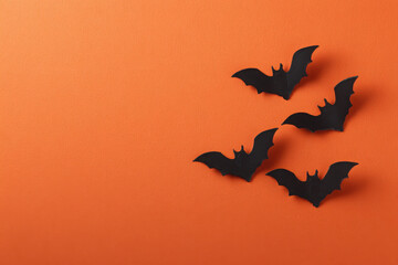 Obraz premium Four black paper bats arranged on a vibrant orange background, symbolizing the Halloween holiday.